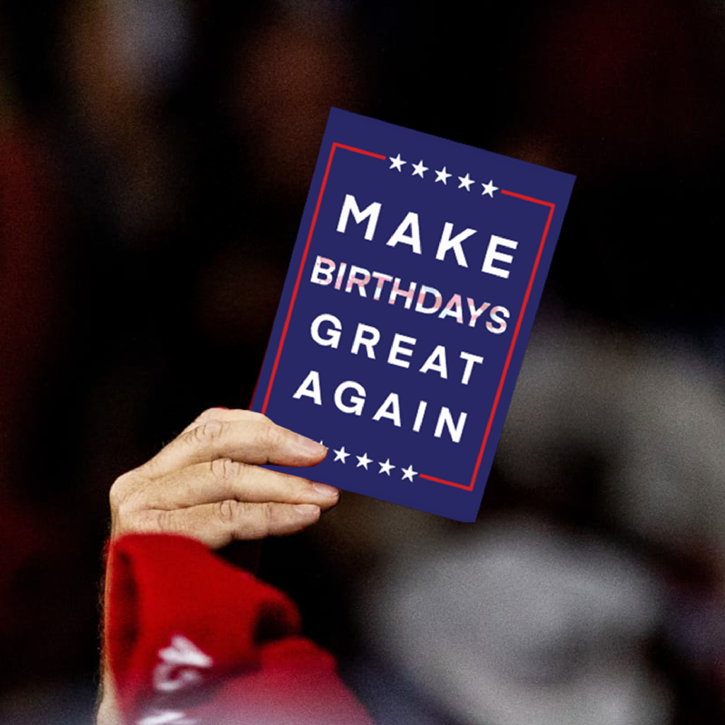 Hand holding a card with 'Make Birthdays Great Again' text against a blurred background