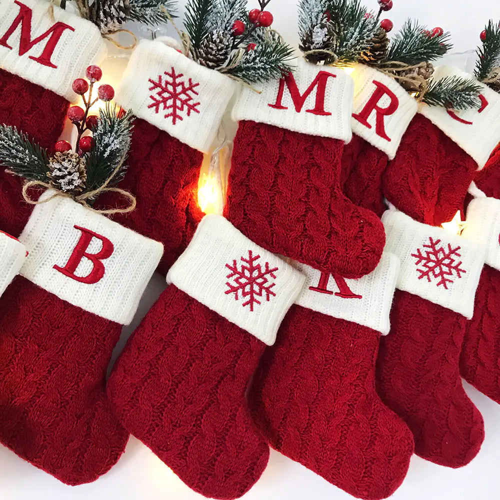 Red Christmas stockings with white trim and lettering, decorated with snowflakes and pine branches.