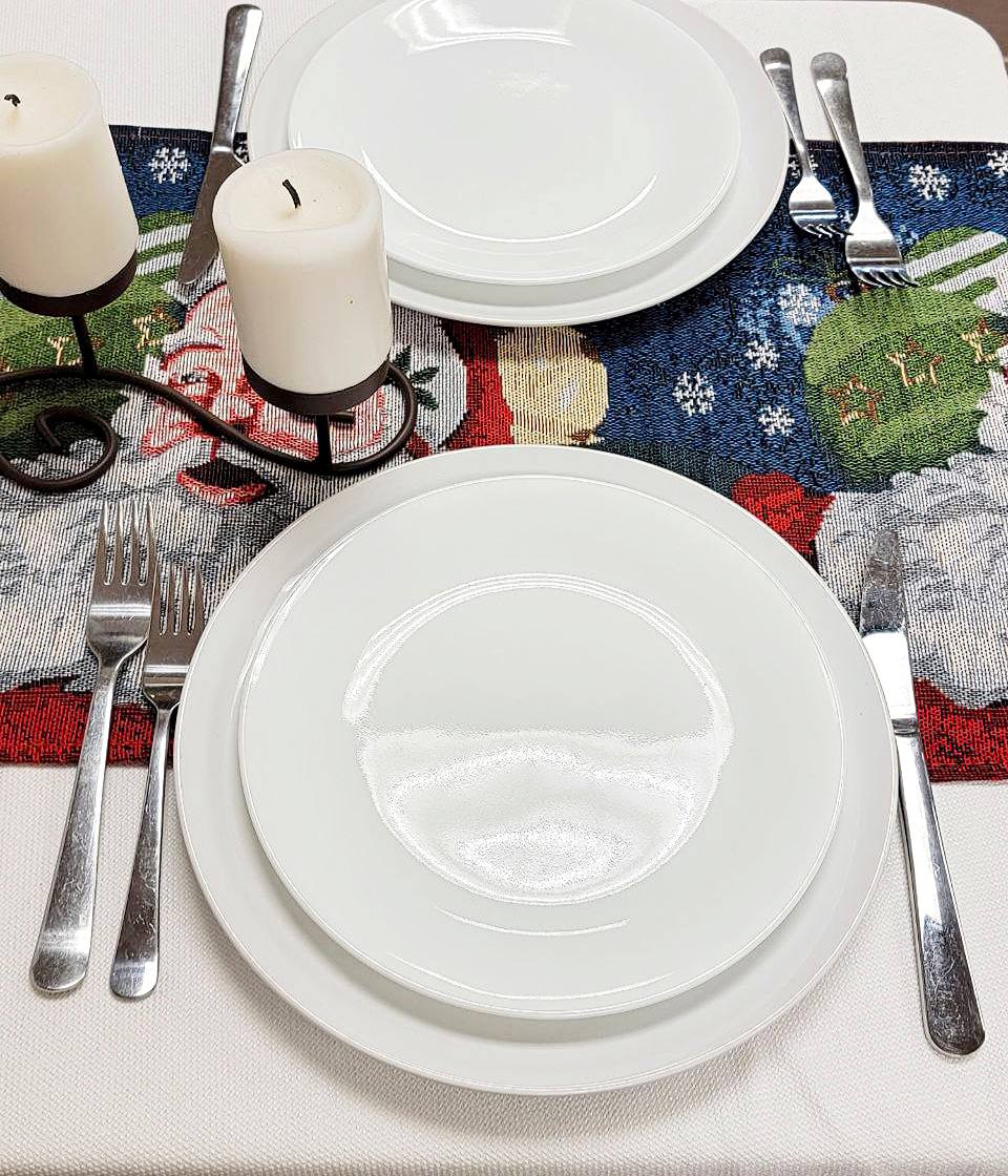 Set table with white plates, silverware, and candles on a decorative tablecloth.