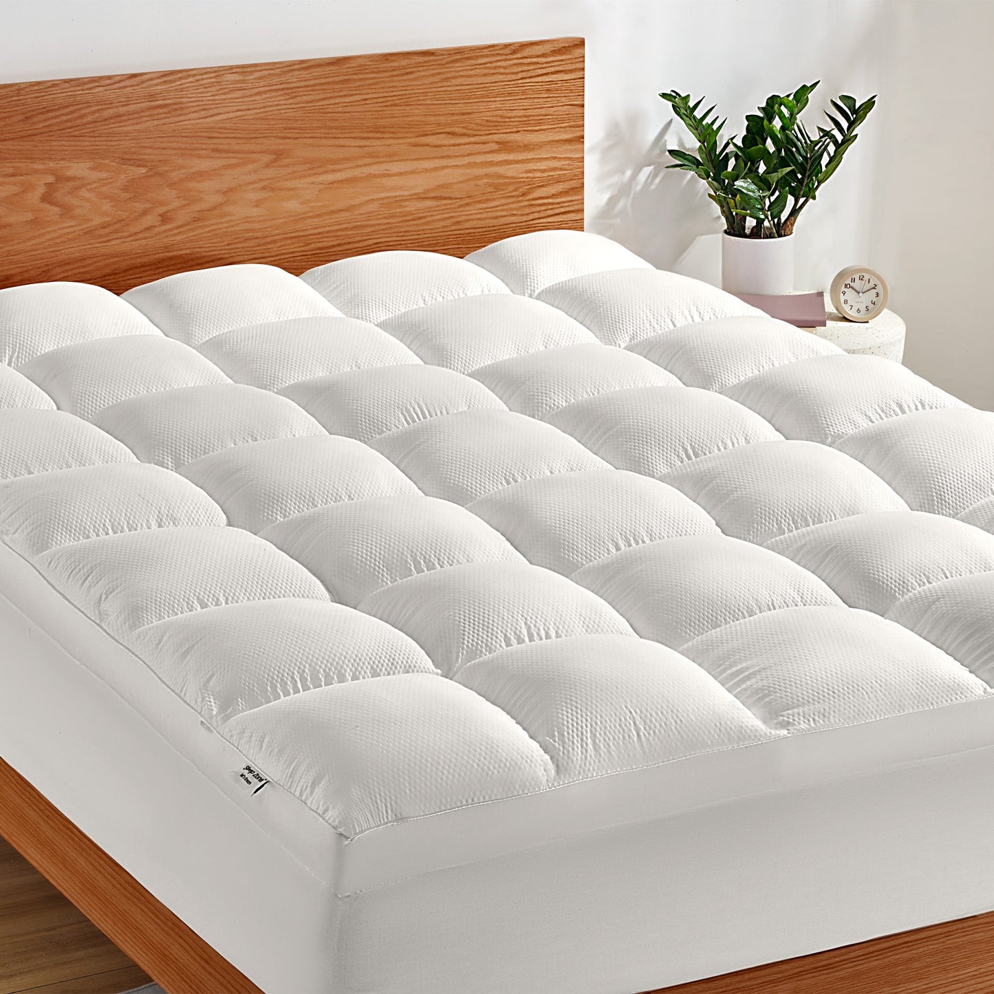 White mattress topper on a bed with wooden headboard and plant in the background