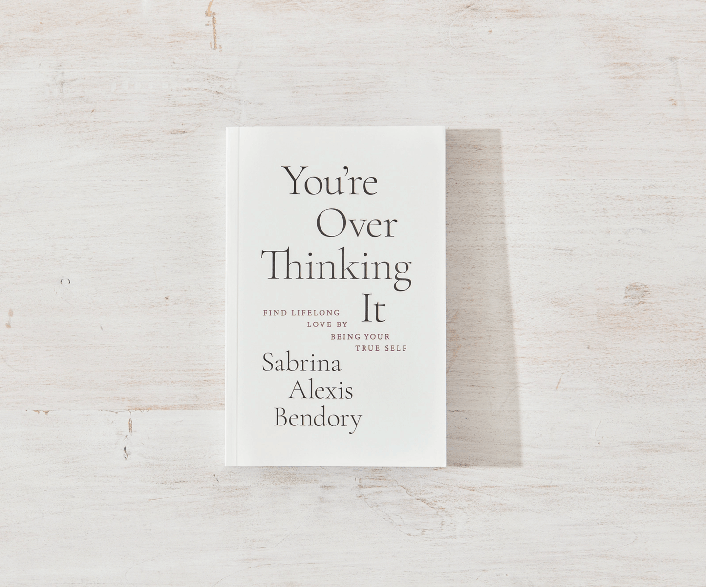Book titled 'You're Over Thinking It' by Sabrina Alexis Bendory on a light wooden surface