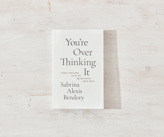 Book titled 'You're Over Thinking It' by Sabrina Alexis Bendory on a light wooden surface