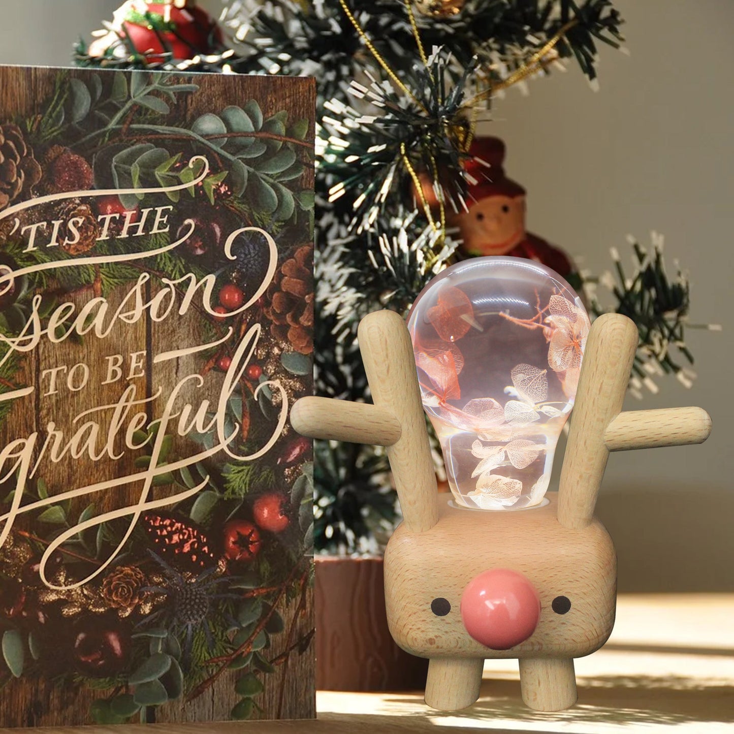 Wooden rabbit figurine with a glass ball, Christmas-themed sign, and decorated tree in the background.
