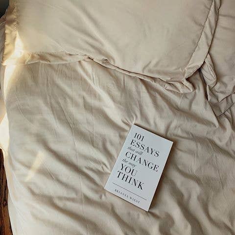 Book titled '101 Essays That Will Change the Way You Think' on a beige blanket