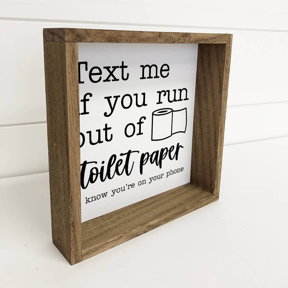 Wooden-framed sign with humorous text about toilet paper on a white background
