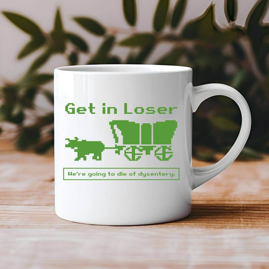 White mug with green text and graphics on a wooden surface with a blurred plant background