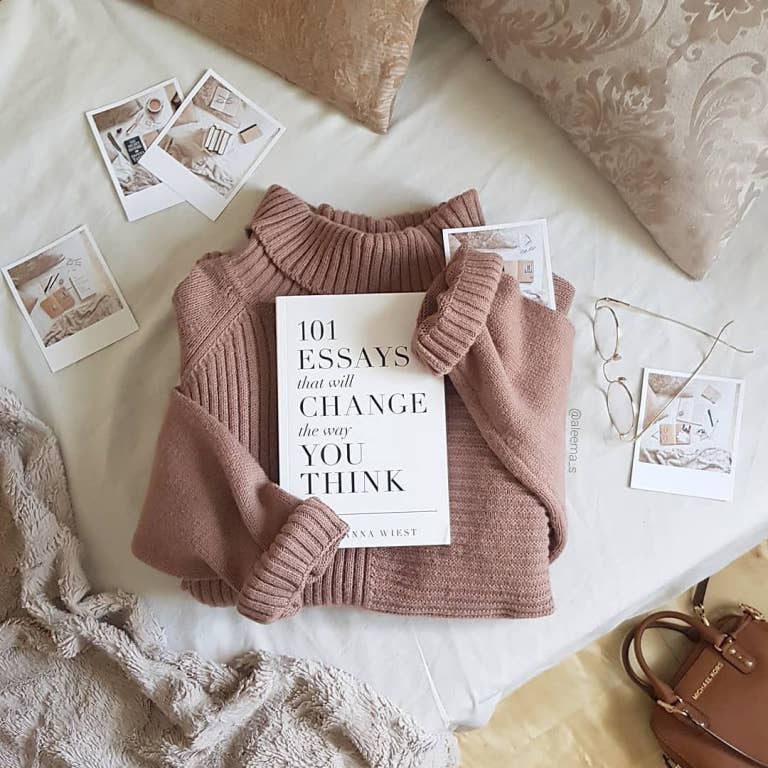 Folded pink sweater with a book titled '101 Essays that Will Change the Way You Think' on a light surface.