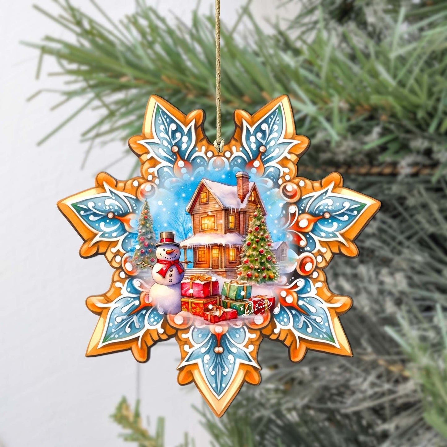 Decorative Christmas ornament with a snowman, house, and tree on a snowflake design against a green tree background.