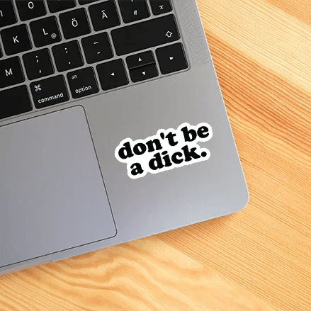 Laptop with a sticker saying 'don't be a dick.' on a wooden surface
