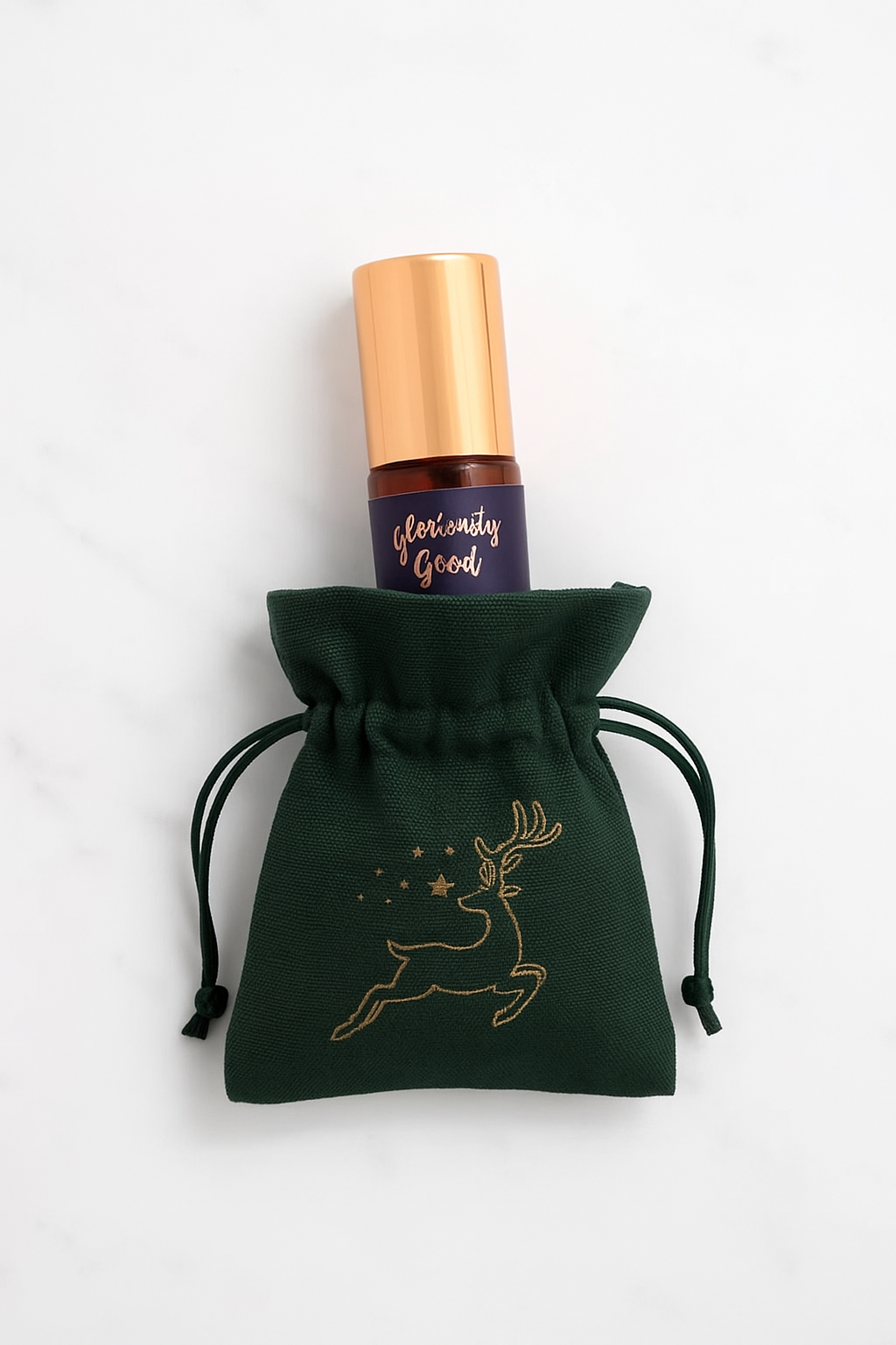 Roll-on bottle with gold cap and dark label on a green drawstring pouch with deer design, against a white background.