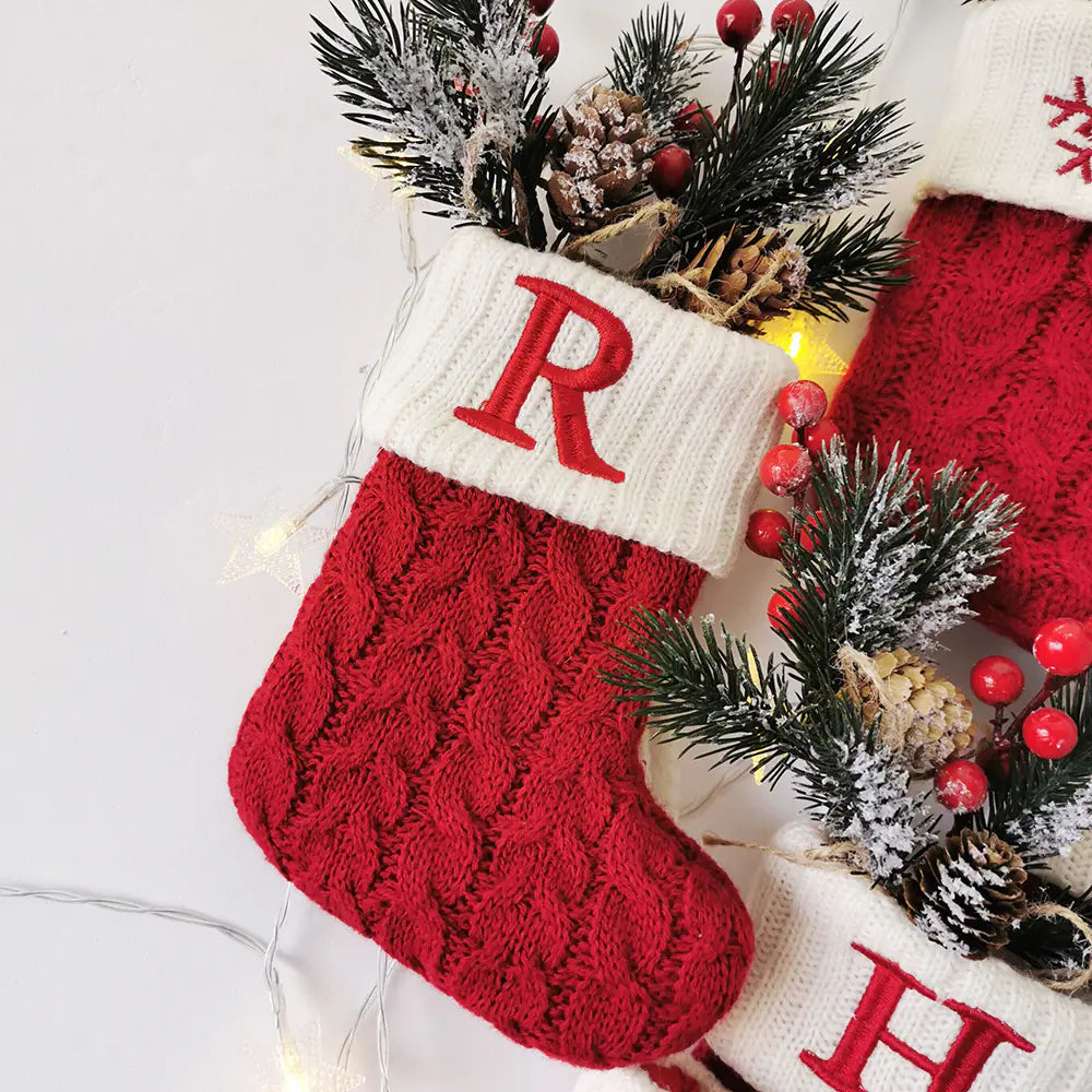 Red Christmas stocking with white cuff featuring a red letter 'R', surrounded by festive decorations.