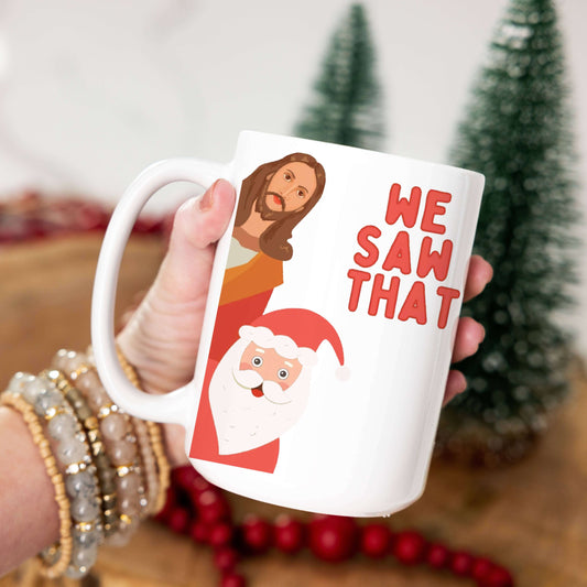 White mug with Christmas-themed design held by a person, with a blurred background of a festive setting.