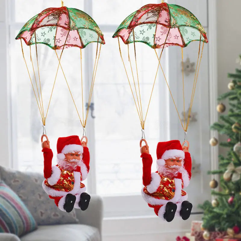 Two decorative parachuting Santa Claus figures hanging against a window with a Christmas tree in the background.