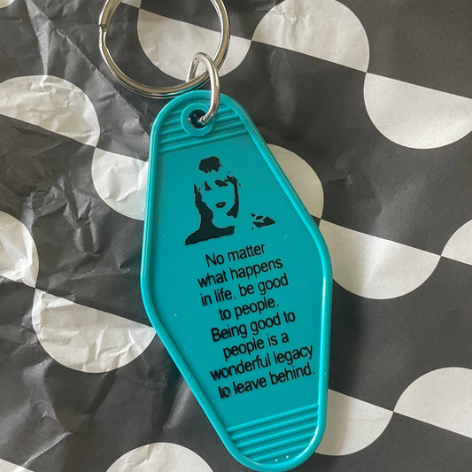 Teal keychain with motivational quote on a black and white patterned background