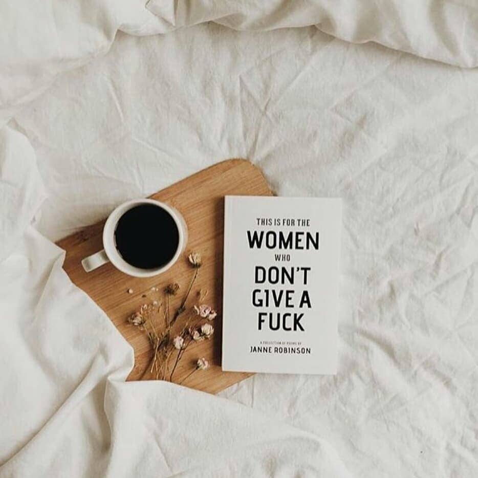 Book titled 'This is for the Women Who Don't Give a Fuck' by Janne Robinson with a cup of coffee on a wooden board.