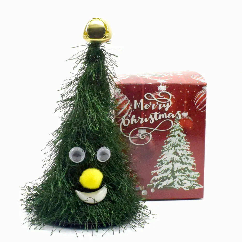 Green Christmas tree-shaped ornament with a gold bell on top, in front of a red 'Merry Christmas' box.