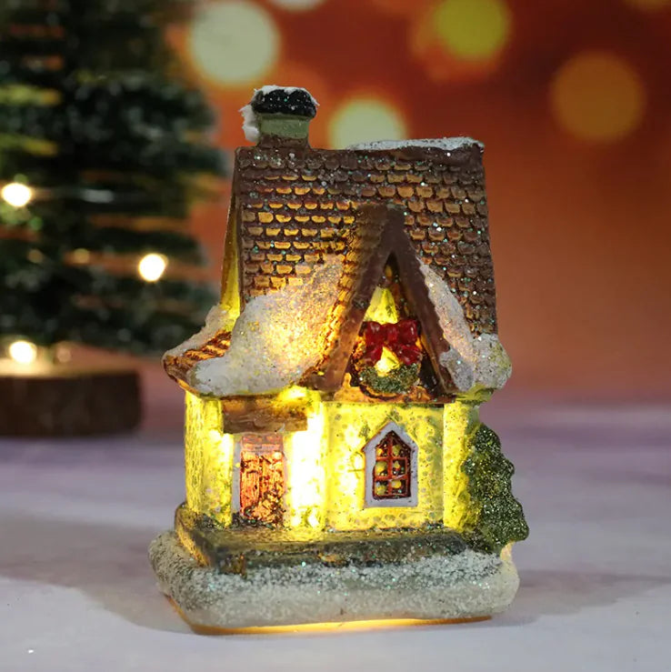Small illuminated Christmas house with a glowing interior, decorated with a bow, on a blurred festive background.