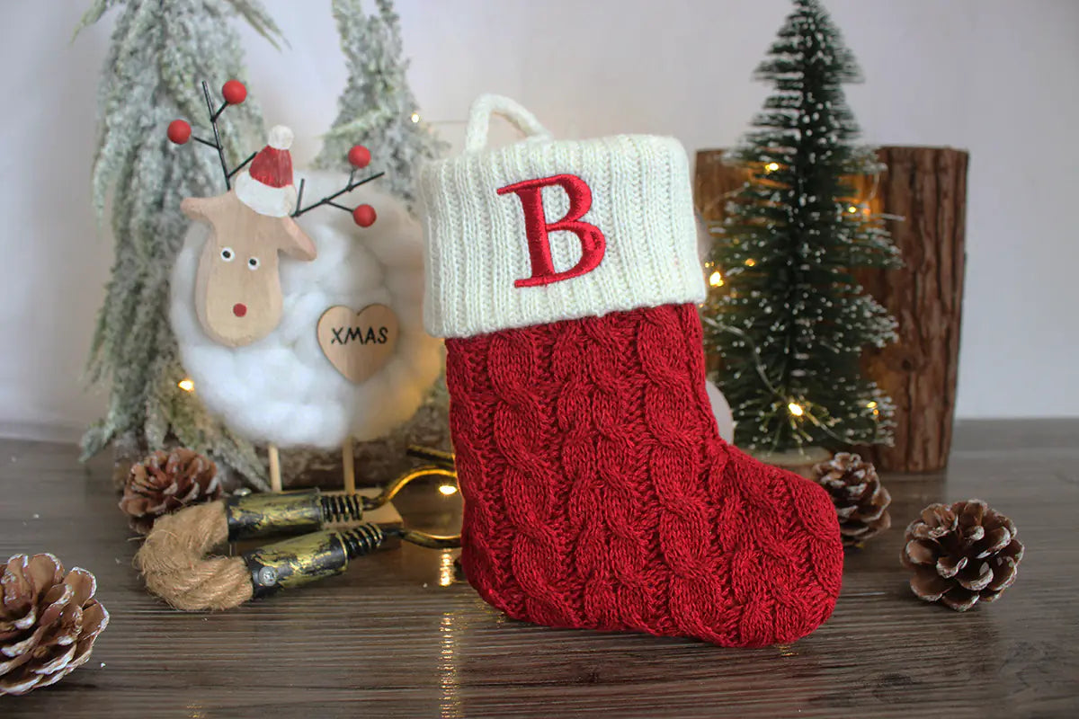 Red Christmas stocking with a white top and red letter 'B' on a wooden surface with festive decorations.