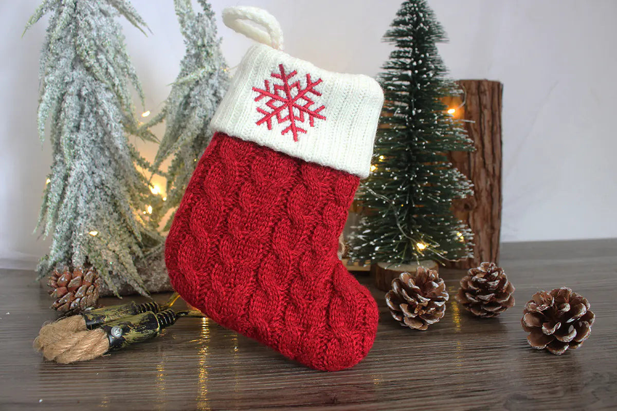 Red knitted Christmas stocking with a snowflake design on a wooden surface with decorative elements.